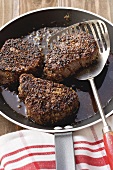 Three peppered steaks in frying pan