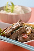 Beef with vegetables & sesame seeds, rice in background (Asia)