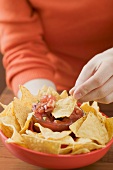 Woman holding bowl of nachos with tomato salsa