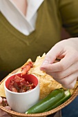 Woman dipping nacho in tomato salsa