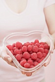 Woman holding heart-shaped container of raspberries