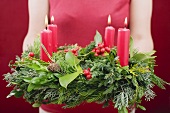 Woman holding Advent wreath with four burning candles