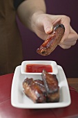 Woman holding glazed pork rib over chilli sauce