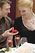 Man giving woman diamond ring over romantic meal