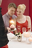 Kellner serviert romantischem Paar Cupcake mit Wunderkerze