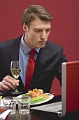 Businessman holding glass of white wine & working at laptop
