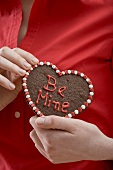 Woman holding chocolate heart with the words Be Mine