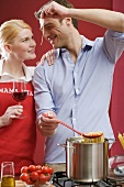 Couple cooking spaghetti & tomatoes, woman holding glass of wine