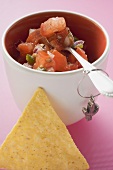 Tomato salsa in pot with spoon, nacho beside it (Mexico)