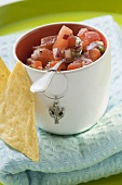 Tomato salsa in pot with spoon, nachos beside it (Mexico)