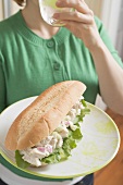 Woman holding tuna sandwich and drinking glass of water