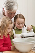 Grandmother and two granddaughters using electric mixer