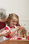Small girl and grandmother decorating gingerbread house
