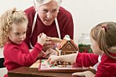 Small girls and grandmother decorating gingerbread house