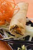 Spring roll on raw vegetables with chopsticks (close-up)