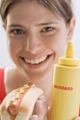 Young woman holding hot dog and mustard bottle