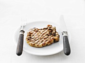 Grilled pork chop on plate with knife and fork