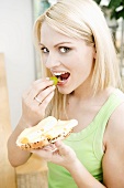 Woman biting into grape and holding cheese sandwich