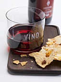 Glass of red wine and crackers on tray, bottle of red wine