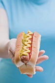 Woman holding hot dog with mustard, relish and ketchup