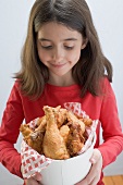 Little girl holding deep-fried chicken drumsticks