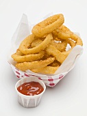 Deep-fried onion rings in paper dish, ketchup beside it