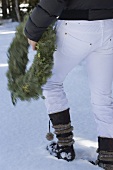 Person trägt Weihnachtskranz im Schnee