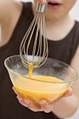 Child holding bowl of egg yolks and whisk