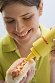 Junge Frau bestreicht Hot Dog mit Senf