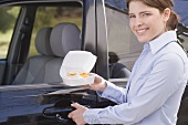 Young woman carrying English muffin in polystyrene box to car