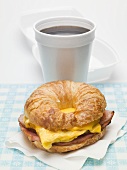 Croissant with scrambled egg, cheese & bacon, cup of coffee