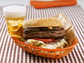 Hamburger and crisps in plastic basket, glass of beer