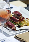 Beef fillet, medium-rare, with potatoes, glass of rosé wine