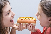 Woman and girl eating the same hot dog from both ends