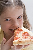 Girl biting into a slice of salami pizza