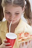 Girl holding slice of pizza and drinking