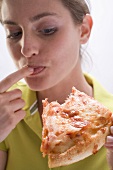 Junge Frau mit abgebissenem Pizzastück leckt sich den Finger