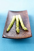 Three spears of green asparagus in wooden dish