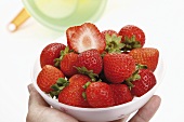 Hand holding strawberries in white bowl