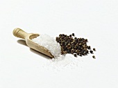 Salt in wooden scoop, peppercorns beside it