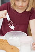 Little girl mixing beaten egg white with icing sugar