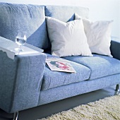 Blaue Couch mit weissen Kissen, Buch und einem Glas Wasser auf der Armlehne