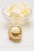 Pieces of butter and butter curls in glass dish, butter curl on bread