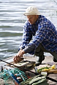 Man grilling fish at water's edge (Sweden)
