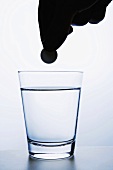 Hand hält Brausetablette über Glas Wasser