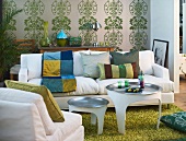Weisses Wohnzimmersofa vor weiss-grüner Wandtapete auf grasgrünem Teppich; davor zwei weiße Tabletttische