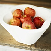 Red apples in white bowl on wooden table