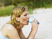 Frau trinkt Glas Wasser am Strand