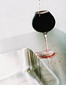 Over-full glass of red wine beside sink