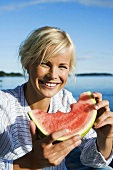 Woman eating watermelon by side of lake